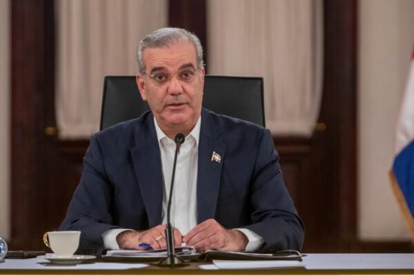 El presidente Luis Abinader habla ante un micrófono sentado en una mesa, con banderas dominicanas al fondo.