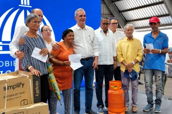 El presidente Luis Abinader posa en una tarima con beneficiarios que sostienen documentos, junto a cajas de estufas de gas y un cilindro anaranjado