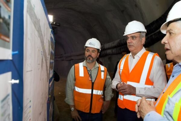 Luis Abinader, con casco blanco y chaleco reflectante, observa planos de obra dentro de un túnel junto a otros dos hombres con equipo de seguridad.
