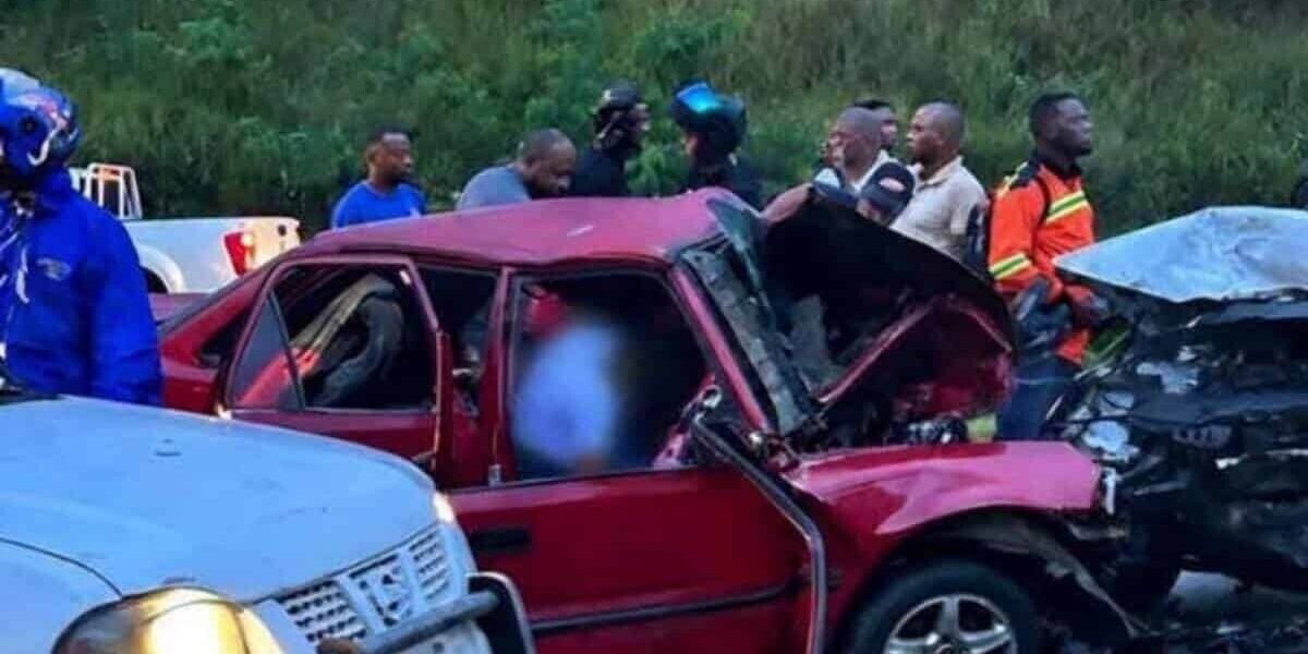 Un automóvil rojo destrozado tras chocar con otro vehículo, rodeado de curiosos y motoristas en una carretera