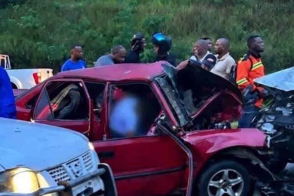 Un automóvil rojo destrozado tras chocar con otro vehículo, rodeado de curiosos y motoristas en una carretera
