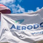 Gobierno reporta RD$9,545 millones ejecutados en obras pagadas por Aerodom Bandera de AERODOM junto a la bandera dominicana en un aeropuerto