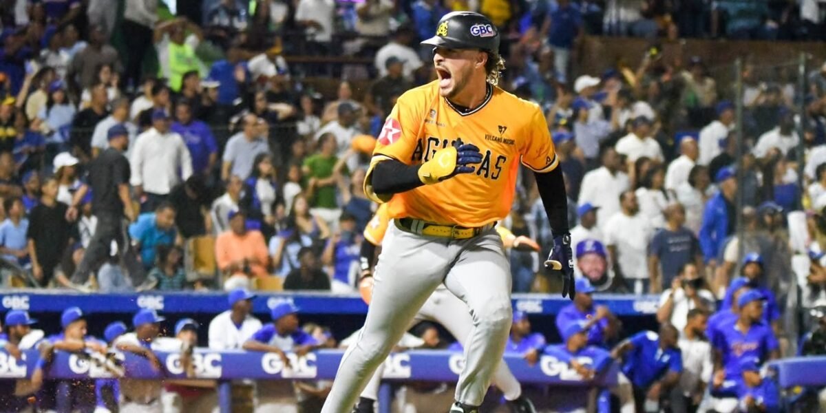 Un jugador de las Águilas Cibaeñas, con camiseta amarilla y casco, grita mientras corre; al fondo, el dugout de los Tigres del Licey y el público en las gradas