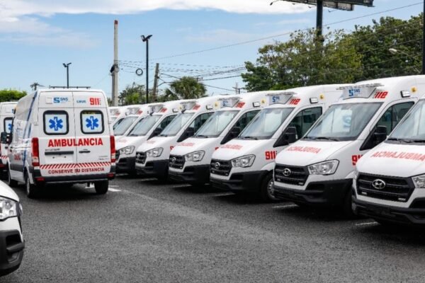 Fila de ambulancias blancas del sistema 911 estacionadas en un parqueo.