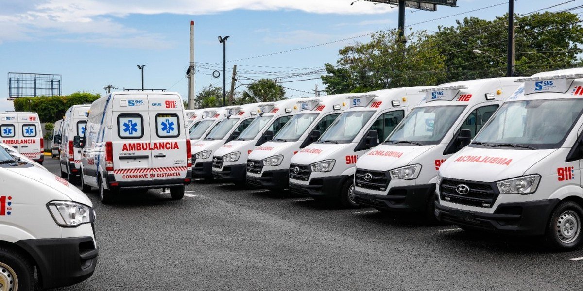 Fila de ambulancias blancas del sistema 911 estacionadas en un parqueo.