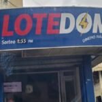 Fachada de una banca de lotería con un letrero azul y la puerta de vidrio cerrada en una calle