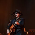 Beto Cuevas, con sombrero y gafas oscuras, canta y toca la guitarra acústica en un escenario