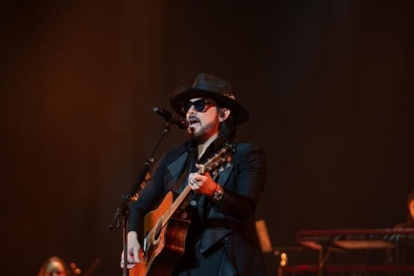 Beto Cuevas, con sombrero y gafas oscuras, canta y toca la guitarra acústica en un escenario
