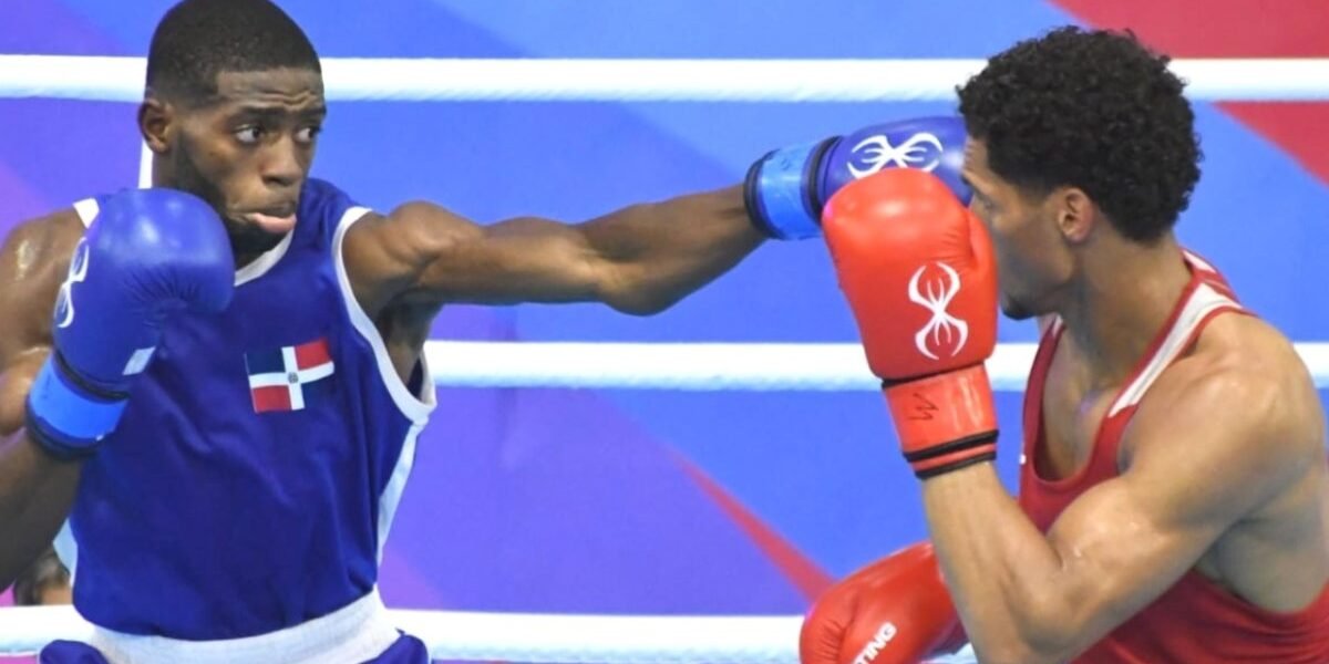 Un boxeador con camiseta azul y la bandera dominicana lanza un golpe a su rival, de rojo, que se cubre con los guantes en el cuadrilátero.