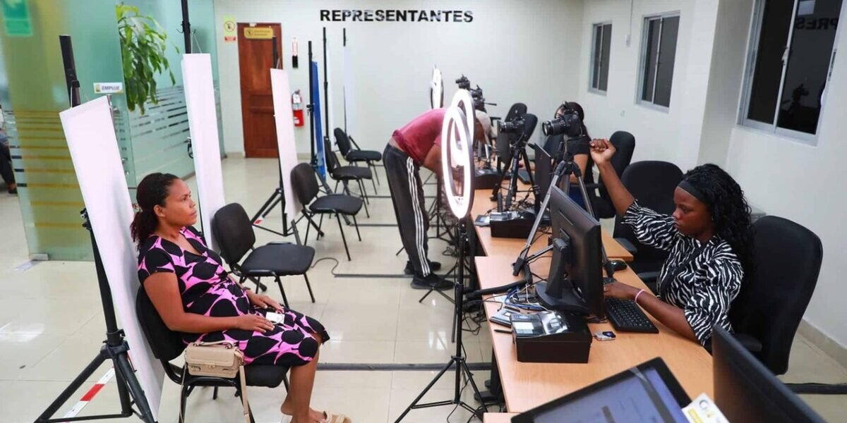 Una mujer sentada frente a un fondo blanco espera su fotografía mientras operadoras trabajan en computadoras con cámaras y aros de luz en un centro de cedulación