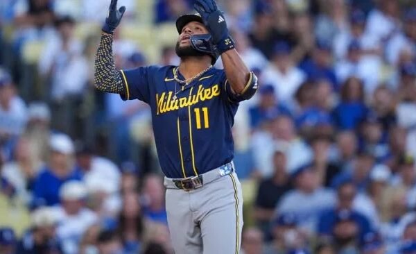 Un jugador de los Cerveceros de Milwaukee con el número 11 levanta los brazos y mira al cielo en el terreno, con el público al fondo