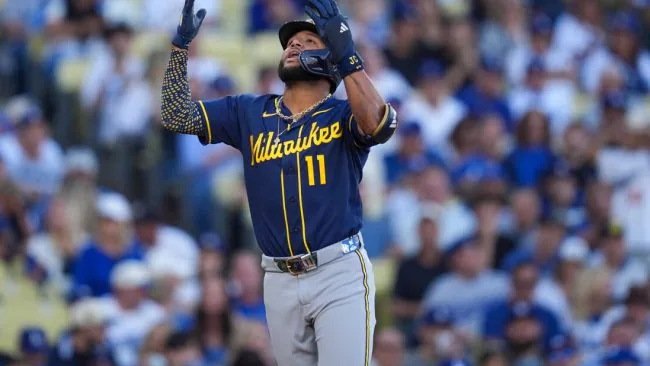 Un jugador de los Cerveceros de Milwaukee con el número 11 levanta los brazos y mira al cielo en el terreno, con el público al fondo
