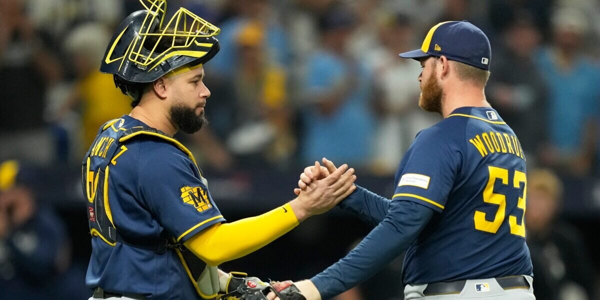 El lanzador de los Cerveceros Brandon Woodruff, con el número 53, choca la mano con su receptor, que lleva careta, en el terreno con el público al fondo