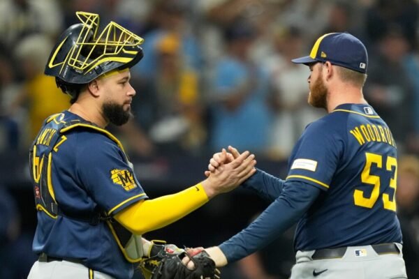El lanzador de los Cerveceros Brandon Woodruff, con el número 53, choca la mano con su receptor, que lleva careta, en el terreno con el público al fondo