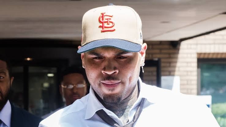 Chris Brown con gorra beige y camisa blanca a la salida de un edificio