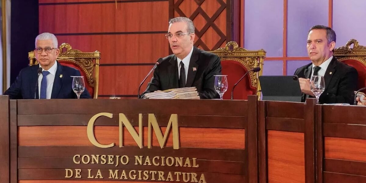 Luis Abinader habla al micrófono en el centro de la mesa del Consejo Nacional de la Magistratura, junto a otros dos miembros del consejo.