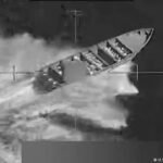 Imagen en blanco y negro de un video militar que muestra una lancha rápida en el mar dentro de una retícula de puntería