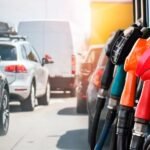Mangueras de surtidores de combustible de colores junto a una fila de vehículos