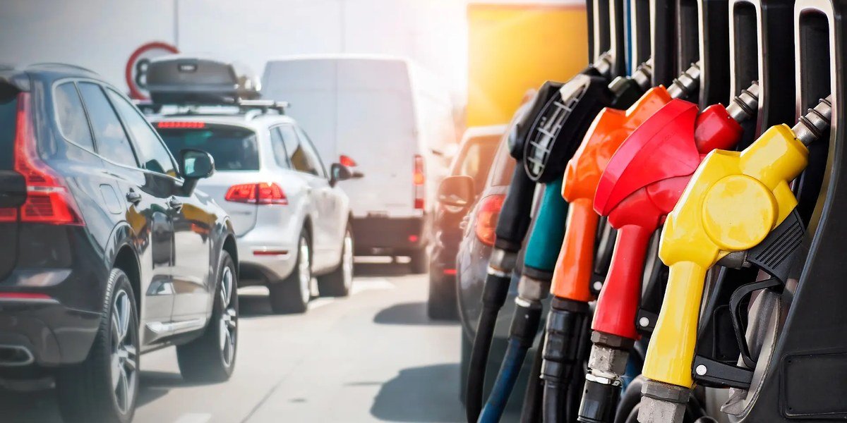 Mangueras de surtidores de combustible de colores junto a una fila de vehículos