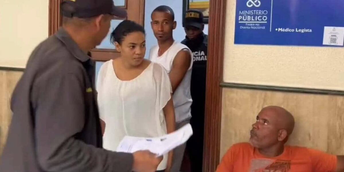 Yokeiry Coronado de la Cruz, de blusa blanca, y Jeider Montero Medina, de camiseta blanca, junto a agentes frente a la oficina del médico legista del Ministerio Público del Distrito Nacional