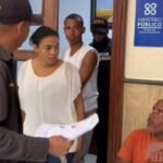 Yokeiry Coronado de la Cruz, de blusa blanca, y Jeider Montero Medina, de camiseta blanca, junto a agentes frente a la oficina del médico legista del Ministerio Público del Distrito Nacional