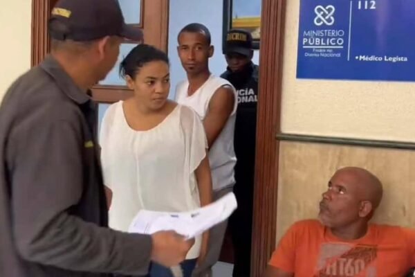 Yokeiry Coronado de la Cruz, de blusa blanca, y Jeider Montero Medina, de camiseta blanca, junto a agentes frente a la oficina del médico legista del Ministerio Público del Distrito Nacional