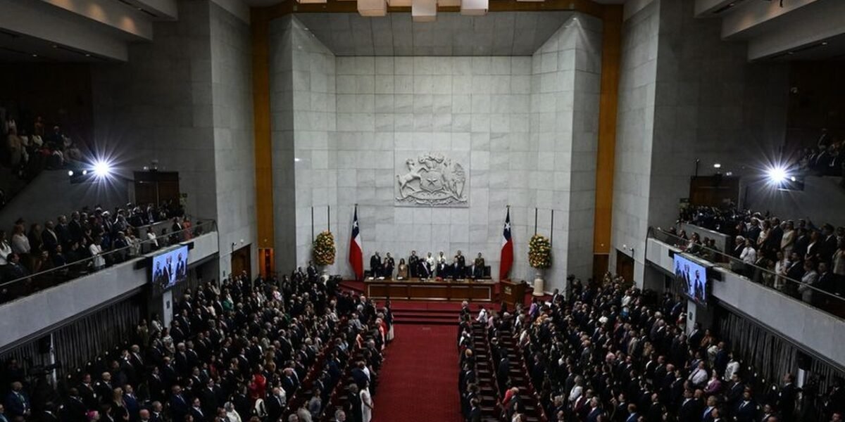 Vista general del hemiciclo del Congreso Nacional de Chile durante una sesión solemne, con el escudo nacional y banderas chilenas al fondo y las tribunas llenas