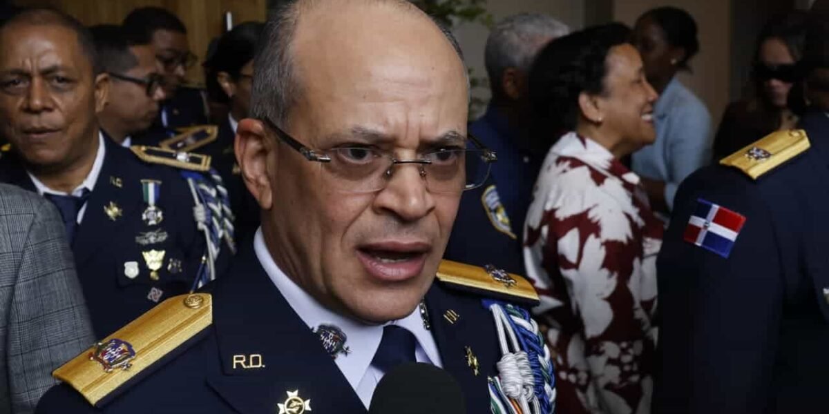 Un oficial de la Policía Nacional con uniforme de gala, lentes y charreteras doradas habla frente a micrófonos de la prensa, rodeado de otros agentes