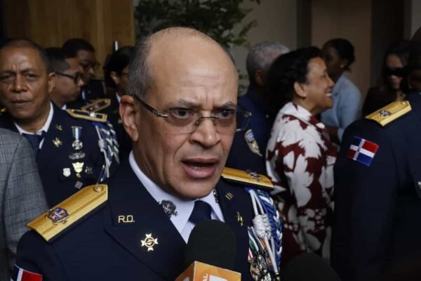 Un oficial de la Policía Nacional con uniforme de gala, lentes y charreteras doradas habla frente a micrófonos de la prensa, rodeado de otros agentes