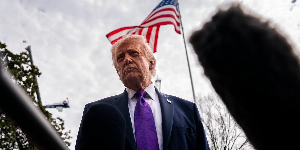 Donald Trump, con corbata morada, frente a micrófonos de la prensa y una bandera de Estados Unidos
