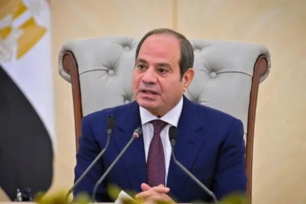 El presidente egipcio Abdelfatah al Sisi habla ante micrófonos, sentado en un sillón junto a la bandera de Egipto