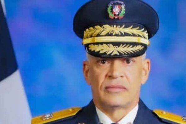 Retrato oficial de Ernesto Rafael Rodríguez García con uniforme de gala y gorra de oficial, junto a la bandera dominicana.