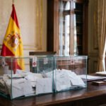 Urnas electorales y bandera de España en entorno gubernamental