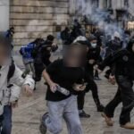 Jóvenes manifestantes, con los rostros difuminados, corren por una plaza entre humo de gas lacrimógeno