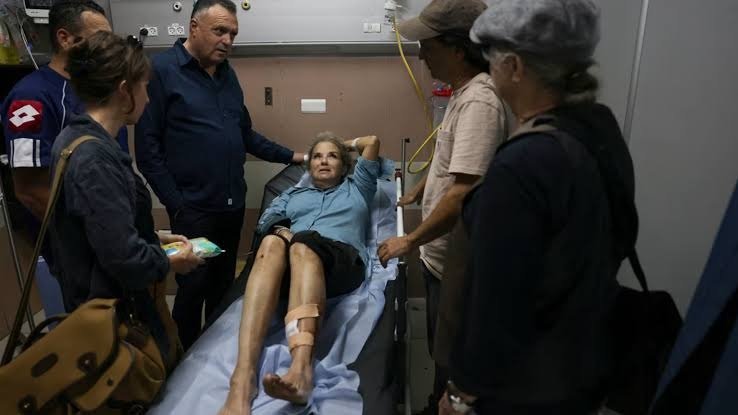 Una mujer con una pierna vendada, tendida en una camilla de hospital, rodeada de varias personas