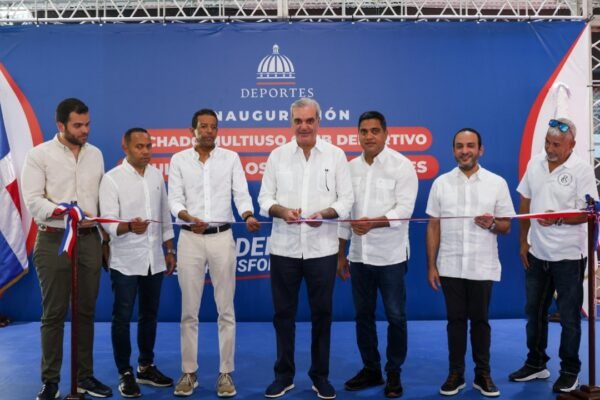 Siete hombres vestidos de blanco cortan una cinta tricolor ante un cartel del Ministerio de Deportes que anuncia la inauguración de un techado multiuso