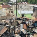 Restos calcinados de viviendas con techos de zinc derrumbados entre casas de bloques; varias personas caminan entre los escombros
