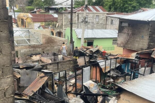 Restos calcinados de viviendas con techos de zinc derrumbados entre casas de bloques; varias personas caminan entre los escombros
