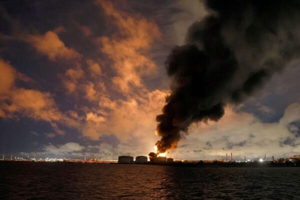 Columna de humo negro y llamas sobre los tanques de una terminal petrolera junto al agua, de noche