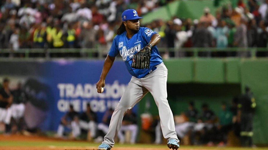 Lanzador con uniforme azul de los Tigres del Licey se prepara para lanzar desde el montículo, con el estadio lleno al fondo.