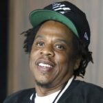 El rapero Jay-Z, con gorra negra y verde, sonríe en un acto público