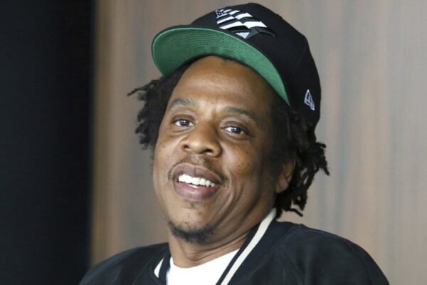 El rapero Jay-Z, con gorra negra y verde, sonríe en un acto público