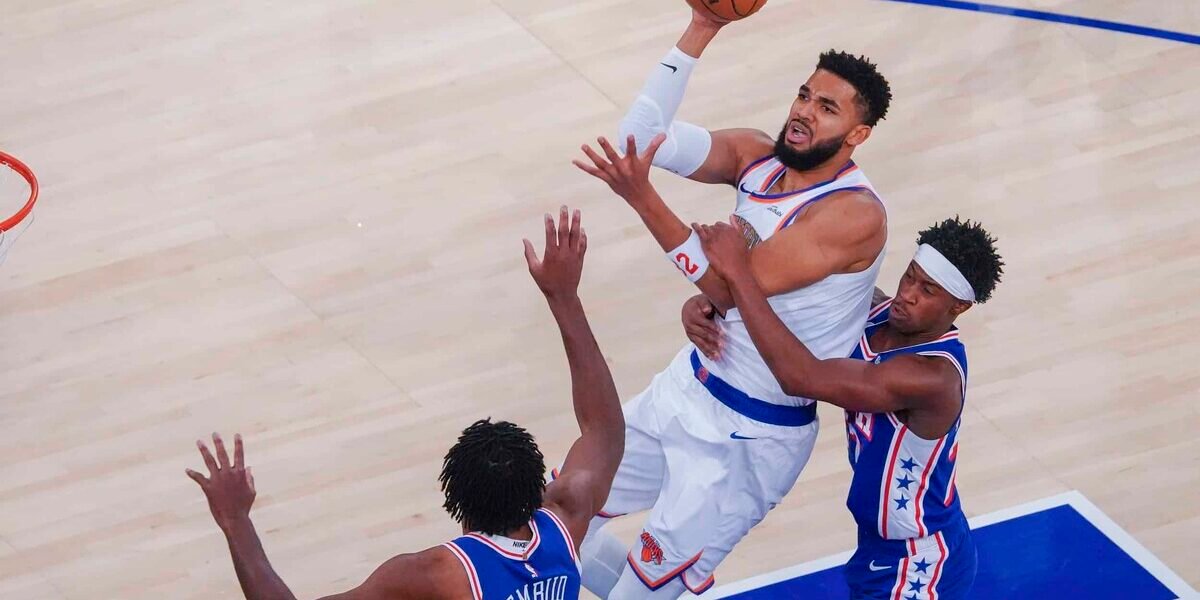 Karl-Anthony Towns, con el uniforme blanco de los Knicks, lanza a canasta entre dos defensores de los 76ers de Filadelfia