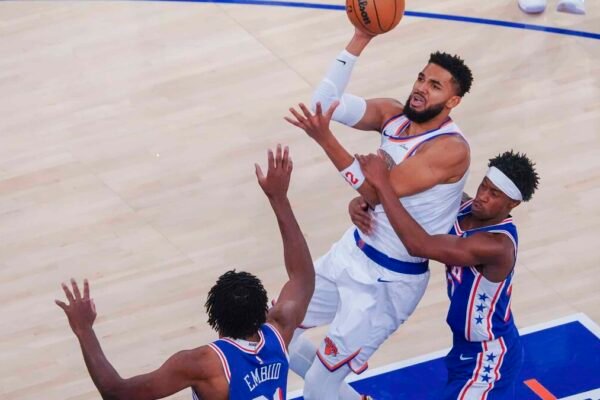 Karl-Anthony Towns, con el uniforme blanco de los Knicks, lanza a canasta entre dos defensores de los 76ers de Filadelfia