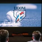 Aficionados de espaldas observan una pantalla con el logo de la Lidom y una pelota de béisbol