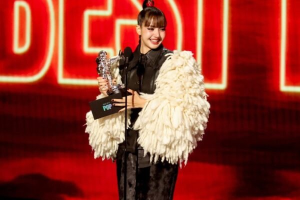 Lisa sonríe en el escenario de los MTV VMA mientras sostiene el trofeo de Mejor Pop, con una chaqueta de flecos blancos