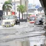 COE levanta las alertas amarillas; 18 provincias y el DN siguen en verde Un camión con grúa, un autobús y varios automóviles circulan por una avenida anegada junto a un paso elevado, bajo un cielo nublado