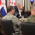 Abinader revela que movilizó fuerzas especiales por un diplomático en Haití El presidente Luis Abinader habla en una mesa frente a varios militares uniformados, con banderas dominicanas al fondo.