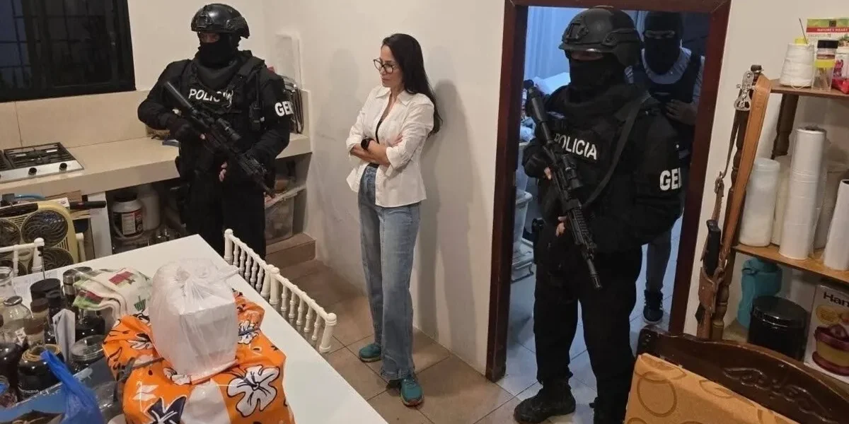 Luisa González, con camisa blanca y jeans, de pie en una vivienda junto a agentes encapuchados de la Policía de Ecuador