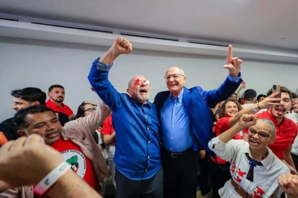Lula da Silva levanta el puño junto a Geraldo Alckmin, rodeados de seguidores con camisetas rojas en un salón